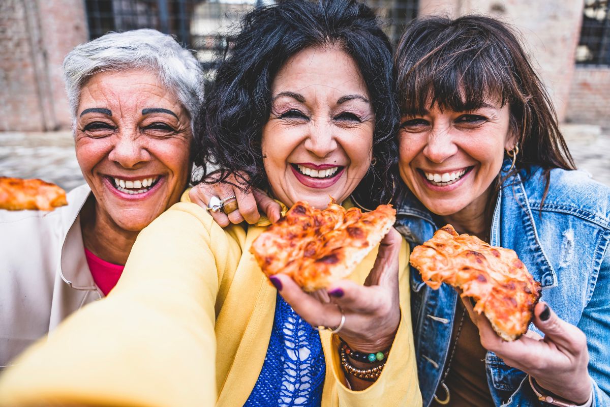 Three mature women smiling and eating pizza.